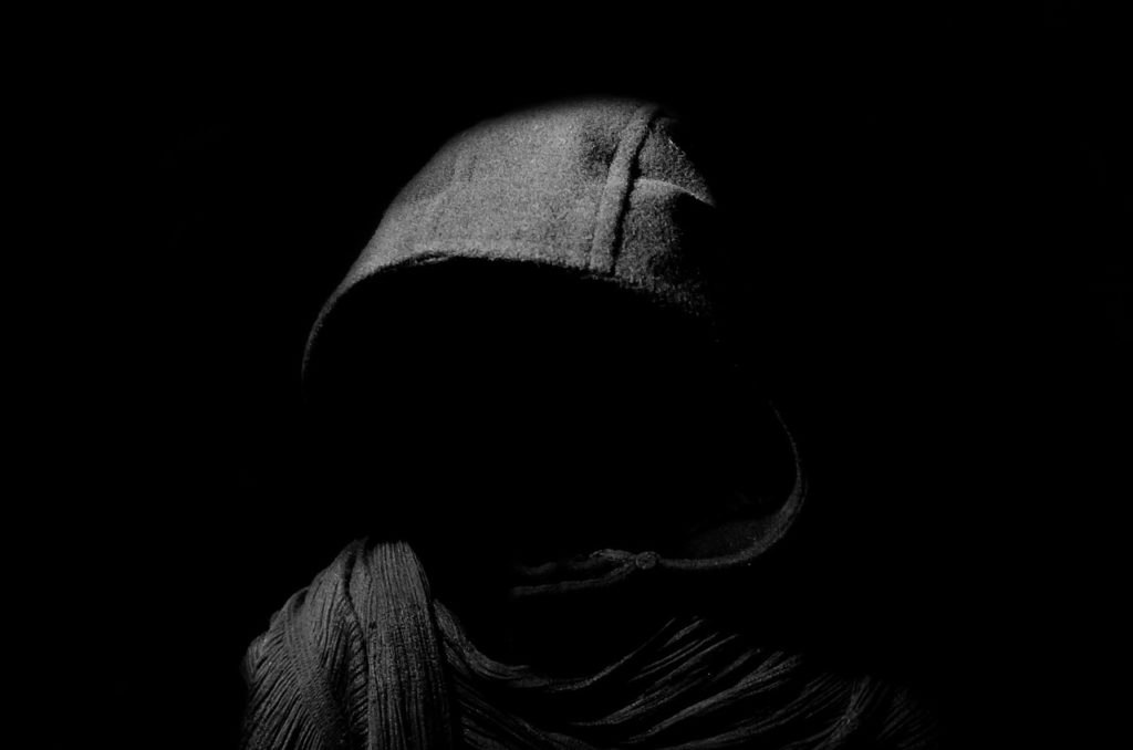 Mysterious dark hooded figure partially lit against a dark background